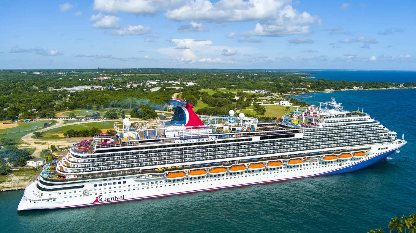 A cruise ship alongside a pier with a green tropical shoreline behind it