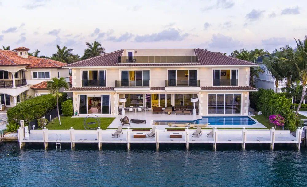Waterfront estate at twilight with a lit pool and private dock, photographed from the air