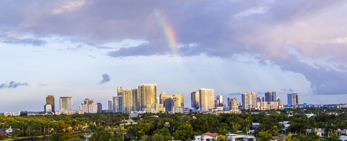 The Fort Lauderdale skyline under a broken sky with a rainbow standing over it