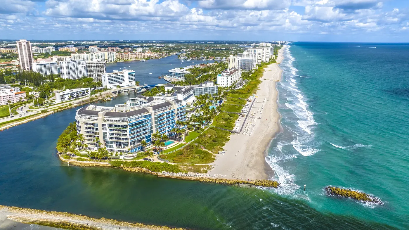 A curving beach and jetty with a modern building on the point and surf running in