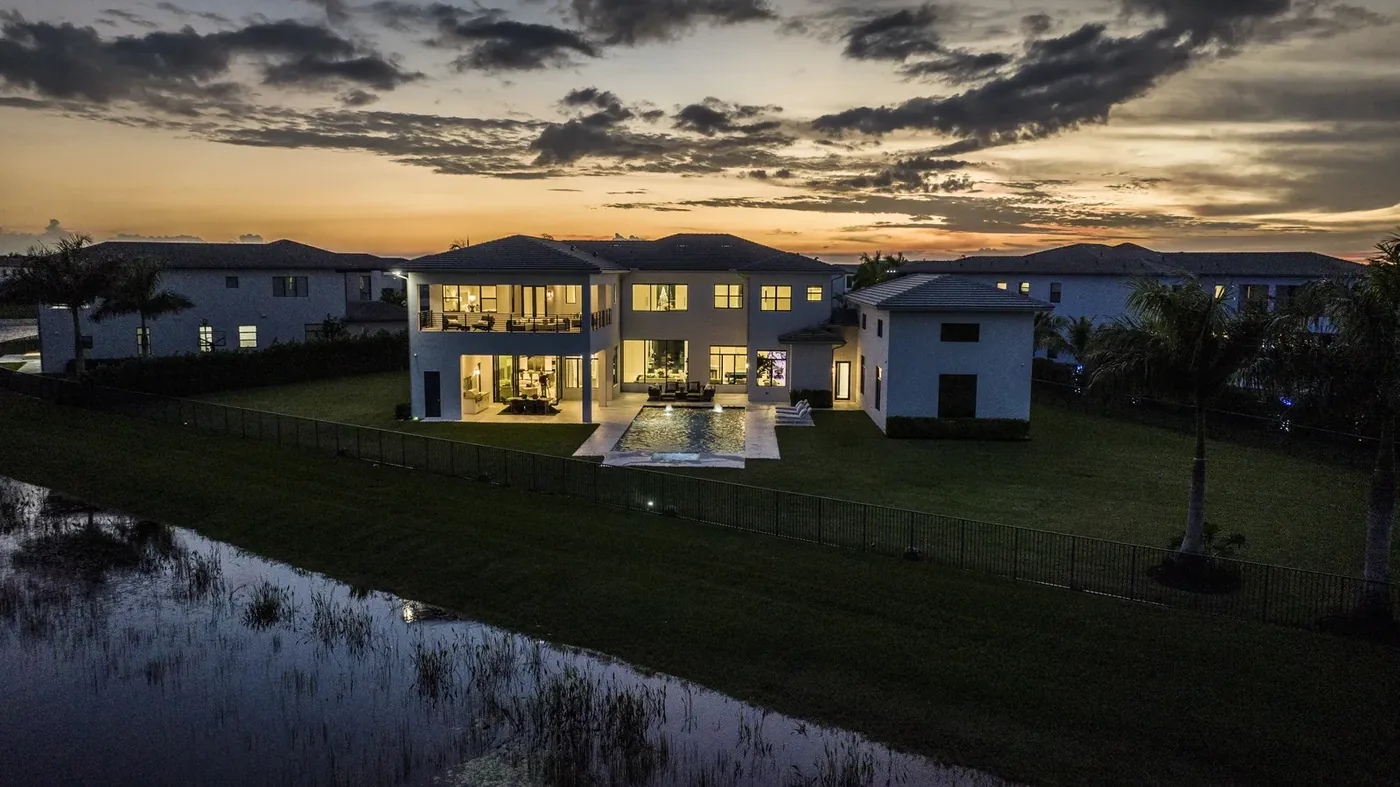 A lit waterfront estate photographed at dusk under a heavy sky