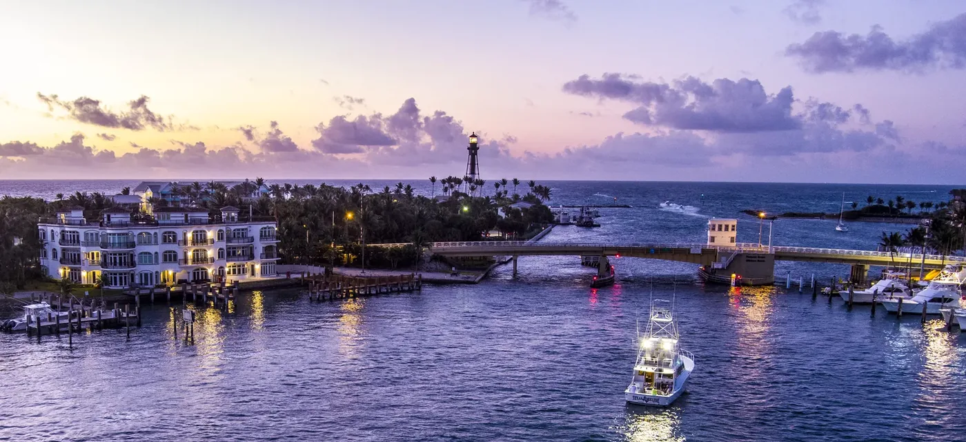 A lighthouse and inlet bridge at twilight with boats working the channel
