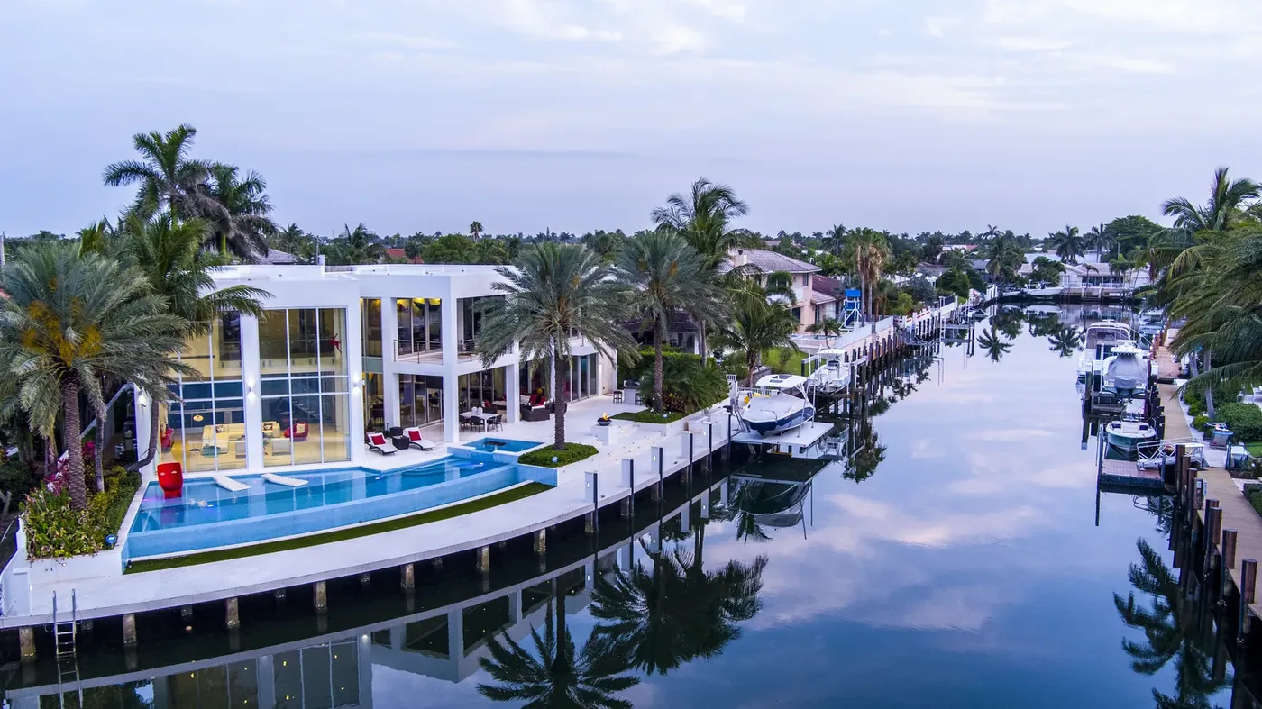 A modern waterfront home with a lit pool and a yacht at its dock
