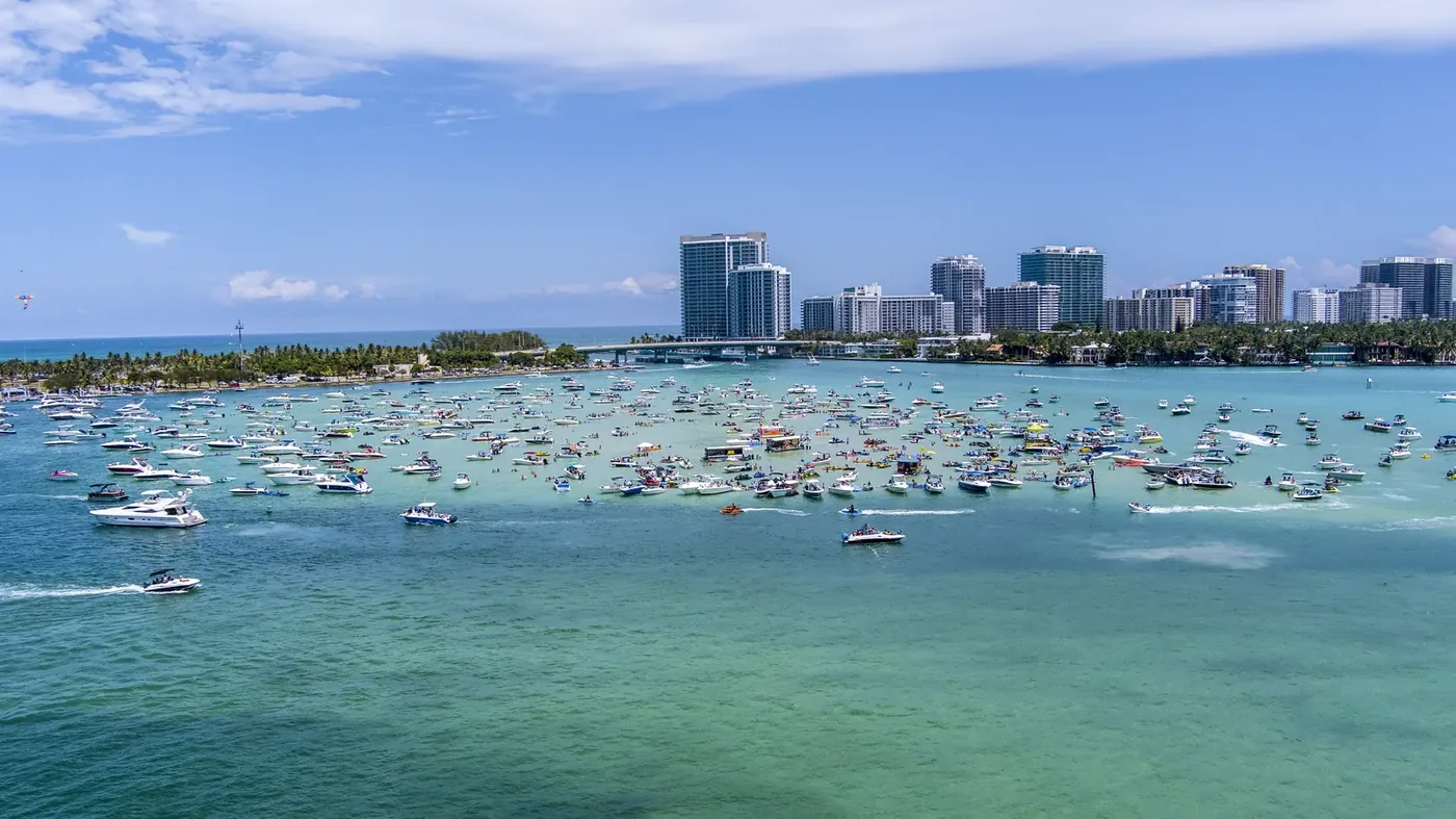 Hundreds of boats rafted up around a sandbar in shallow turquoise water