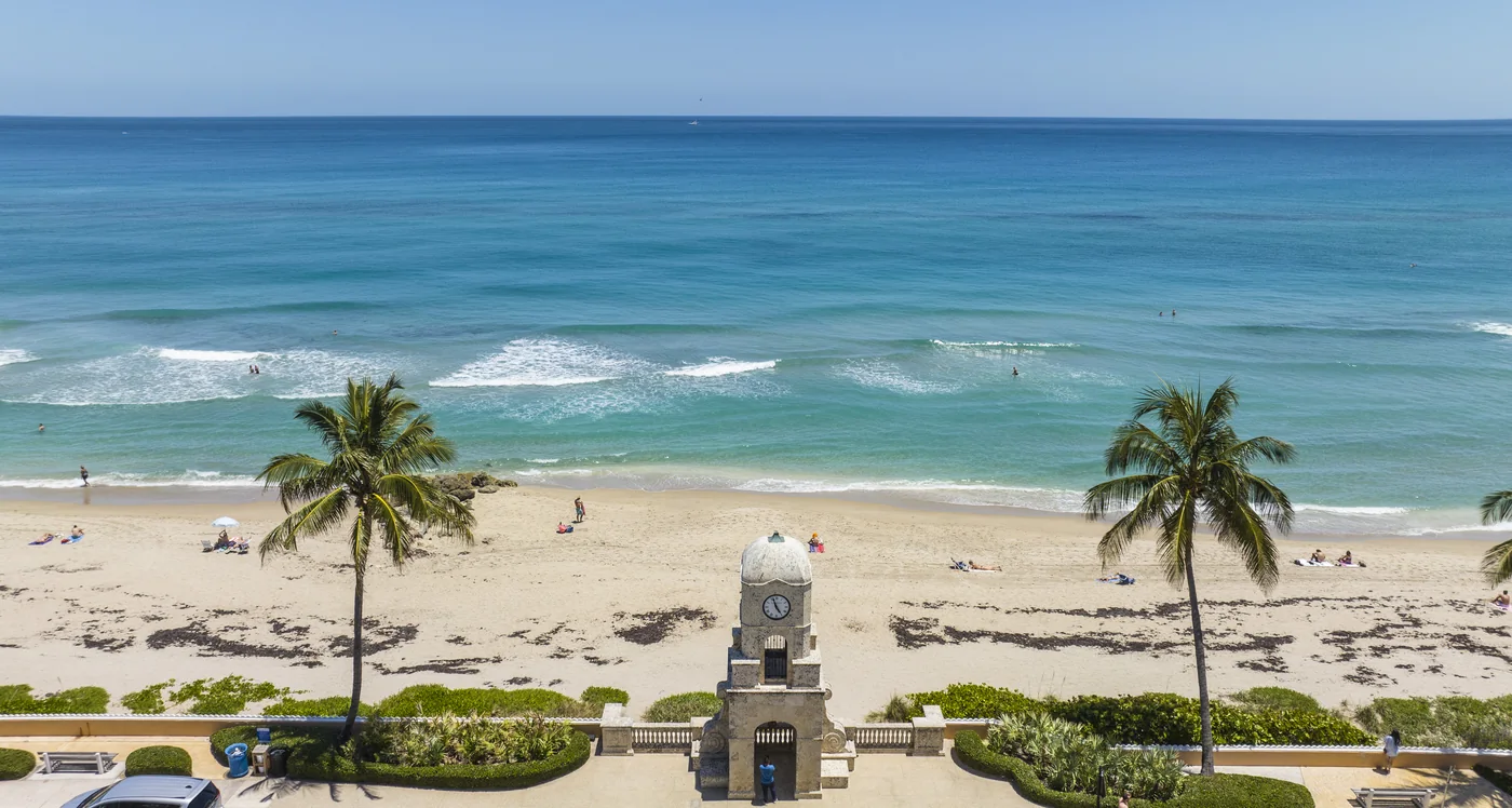 A stone clock tower at the beach end of the avenue framed between two palm trees