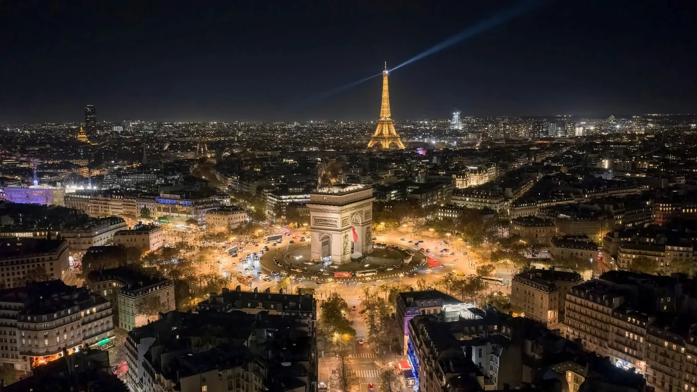 The Arc de Triomphe and a lit Eiffel Tower from the air over Paris at night