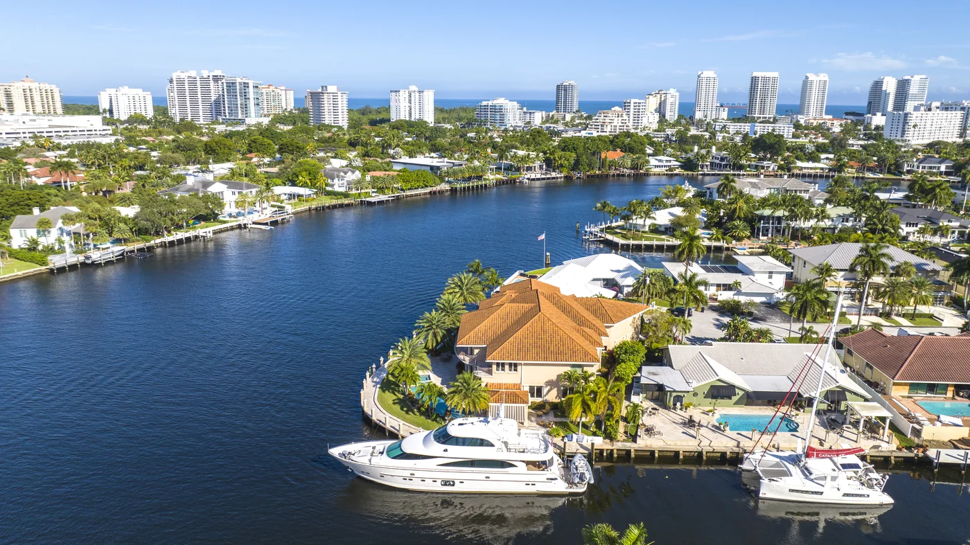 Waterfront estate on the Intracoastal with a motor yacht and a catamaran at its dock, Fort Lauderdale high-rises and the ocean beyond