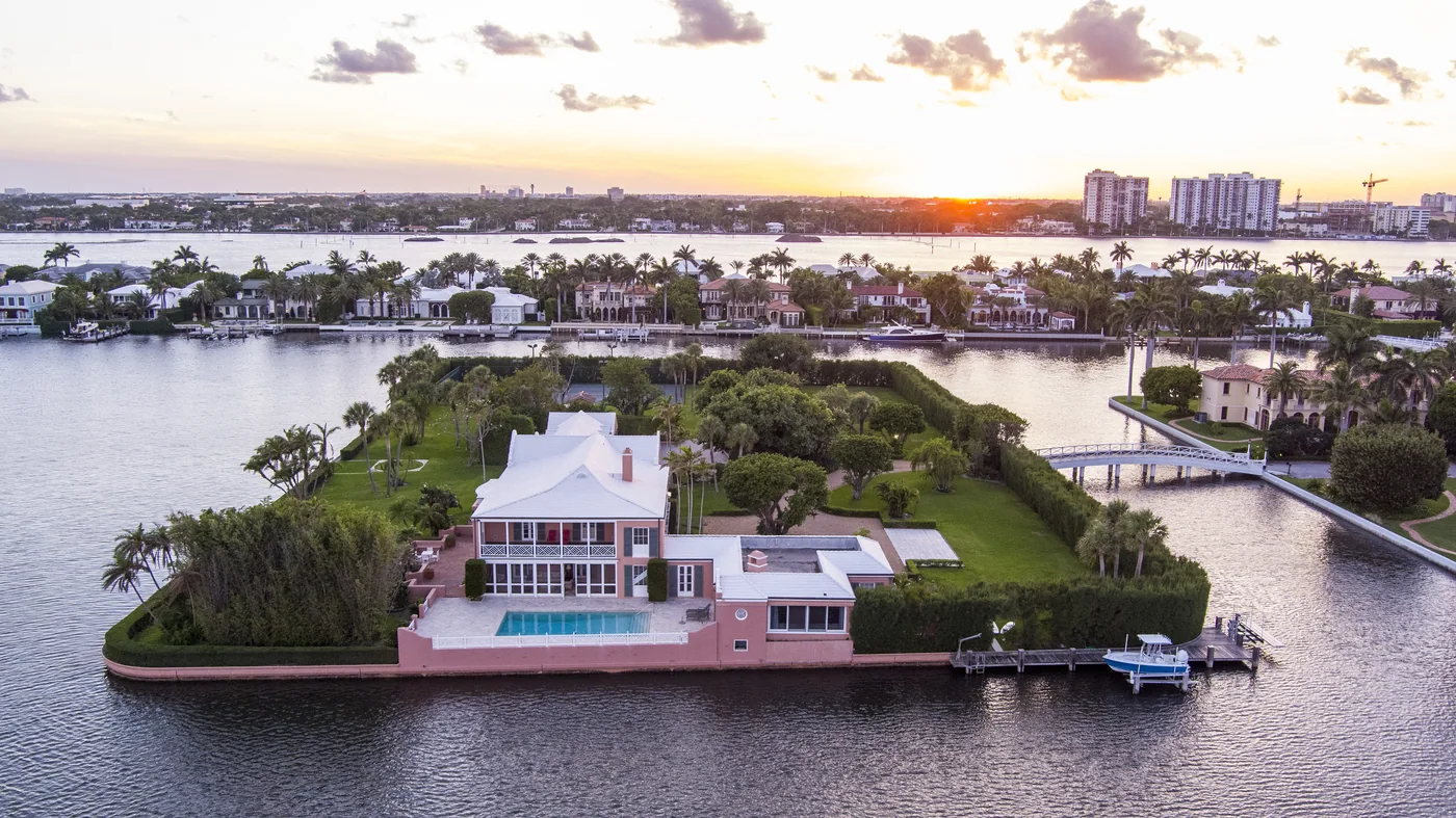A single house on a private island at sunset with a lit pool and a causeway to the mainland