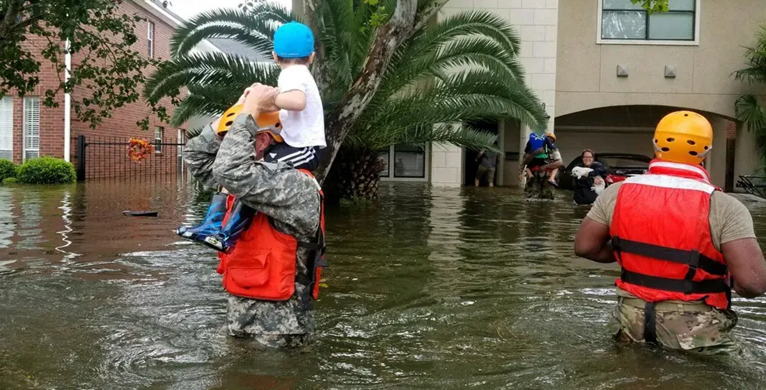 Emergency responders wading through floodwater beside a rescue boat