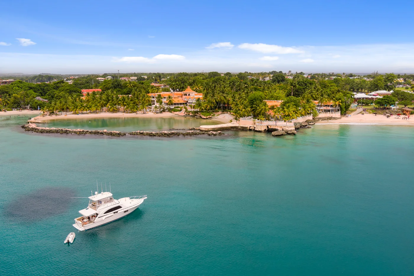 A sportfishing boat anchored over sand in clear green water off a palm-lined shore in Tobago