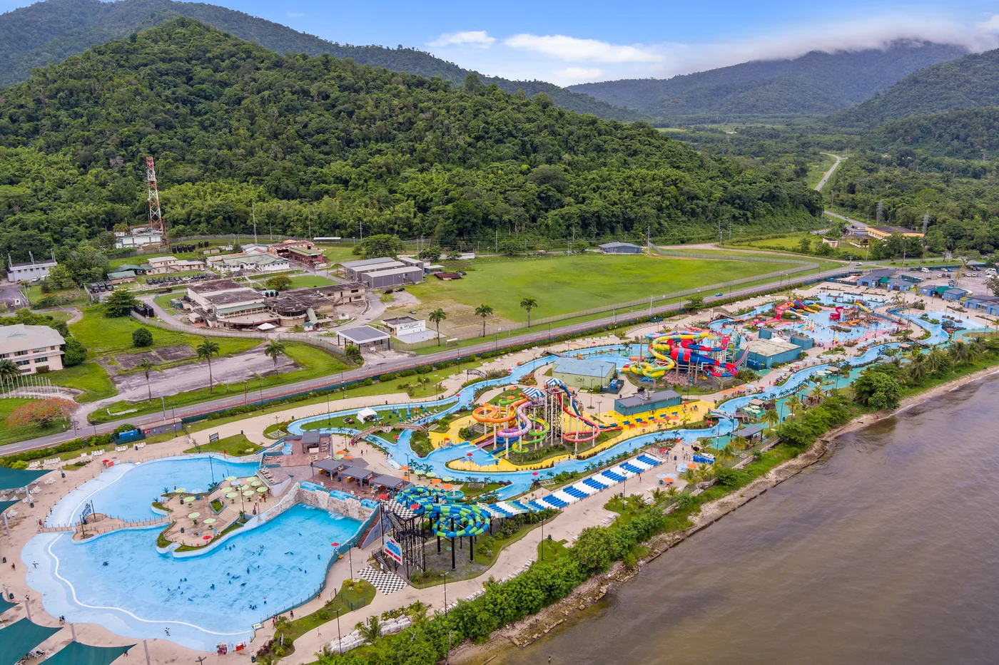 A water park of slides and pools along a river bank with forested hills rising behind